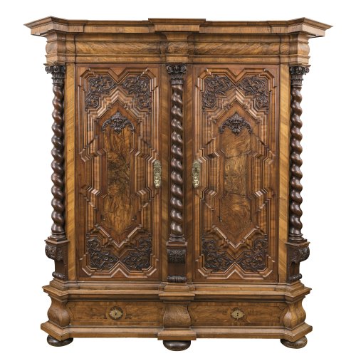 Fassadenschrank. Augsburg, um 1700. Nussbaum, furniert, gedrehte Säulen und Schnitzauflagen. Alterungsspuren, erg. 226 x 219 x 80 cm.