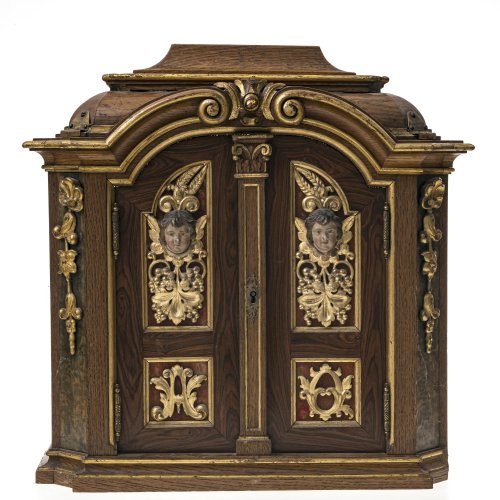 Tabernakelkästchen. Deutsch. Holz, furniert, plastischer Engelskopfdekor. Ohne Schlüssel, Rückwand  und Teile fehlen, Alterungsspuren. 45 x 49,5 x 32 cm.