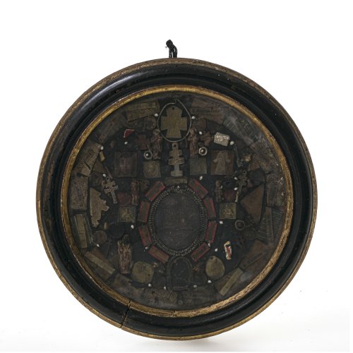 Wettersegen. Süddeutsch, 18. Jh. Im Zentrum Wachsmedaillon, umgeben von Reliquienpartikeln, Gnadenbildern, Siegeln und Naturalien.  Besch., Alterungsspuren. ø 20,5 cm, mit Rahmen ø 24 cm.