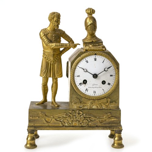 Französische Kamin-Pendule. Paris, um 1820. Kaminuhr in Miniatur. Bronze, feuervergoldet. Darstellung eines Reitersoldaten, der auf einen Federbuschhelm und Sporen auf  einem Kissen zeigt. 