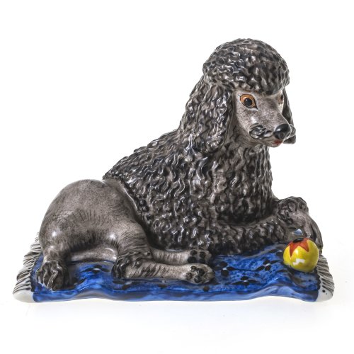 Nymphenburg, ca. 1950-59.  Stattlicher Königspudel auf Teppich mit Spielball. Porzellan, farbig staffiert. Ca. 7,7 x 9,5 x 6,5 cm. Minim. Abrieb.