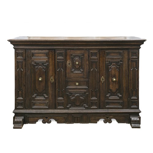 Anrichte. Italien, im Stil des 17. Jh. Eiche, massiv.  Zweitürig, Türfüllungen geschnitzt. Mittig eine kleine Türe, darunter ein Schubfach. Herstellung unter der Verwendung von teilweise alten Holzbrettern, Rückwand neuzeitig ergänzt. Beschläge und Schlösser teilw. ergänzt. 117 x 180 x 56 cm. Rest., besch. Zwei Schlüssel.