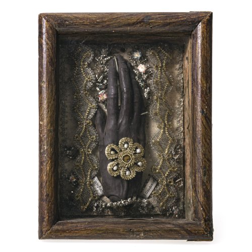 Böhmen oder Wien, 18./19. Jh.  Klosterarbeit mit Reliquien umgeben von Metall- und Golddrahtarbeit. Mittig die Berührungsreliquie Annahand, wohl aus geschwärztem Wachs. 21,5 x 16,5 cm. Deckel lose.