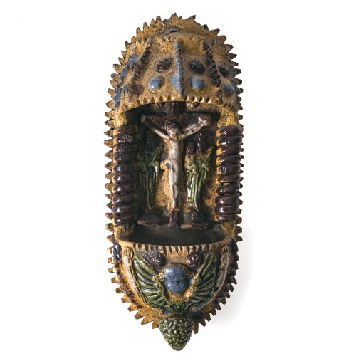 Weihwasserwandbrunnen. Niederbayern. Irdenware, farbig glasiert. Christus am Kreuz, rechts und links jeweils das Gnadenbild von Altötting. Besch. (einige Zacken am Rand fehlen). H. 22 cm.