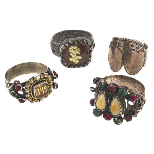 Vier Ringe. Silber, Metall. Zwei mit Goldeglomisé, ein Verlobungsring mit Krone, einer mit Glasstein- und Grandelnbesatz. Ein Anhänger fehlt, einer besch.