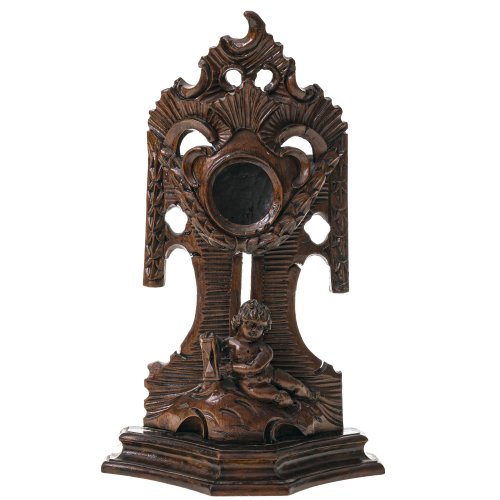 Taschenuhrenständer. 18./19. Jh. Holz, geschnitzt, dunkelbraun gebeizt. Im Vordergrund Junge mit Stundenglas, Empirefeston und Rocailleteilstück. Alterungsspuren, rep. H. ca. 30 cm.