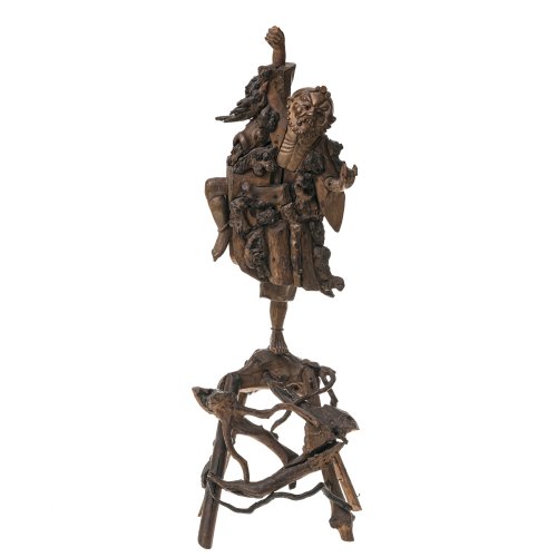 China. Figur eines Wächters der Gottheit Shoulao, Wurzelholz. Schnitzerei aus mehreren Segmenten zusammengesetzt. Zwei Teile, Figur auf Holzgestell. Gegenstand in rechter Hand, fehlt. Teilw. besch. H. ca. 66,5 cm.