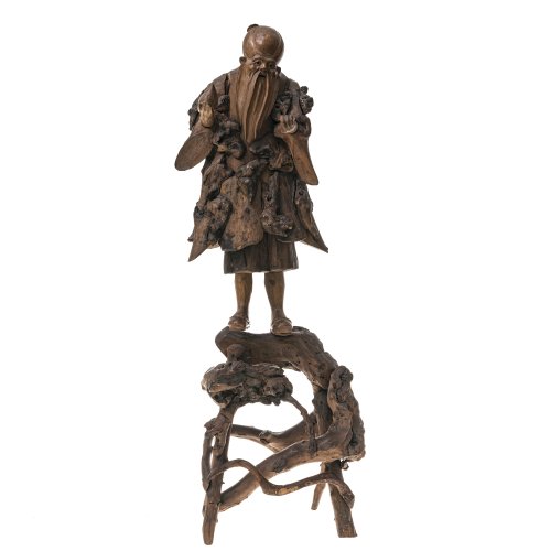 China. Figur des Gottes Shoulao, Wurzelholz. Schnitzerei aus mehreren Segmenten zusammengesetzt. Zwei Teile, Figur auf Holzgestell. Eingesetzte Glasaugen, eines fehlt. Teilw. besch., Daumen fehlt. H. ca. 60,5 cm.