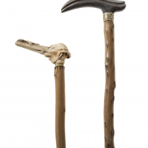 Zwei Spazierstöcke. Griff aus Hirschhorn in Form eines Mischwesens mit menschlichem Kopf und langem Schnabel, auf dem eine Kröte sitzt, der andere Griff aus Steinbockhorn mit Messingmanschette. Schuss jeweils aus Astholz. H. 82-87 cm.