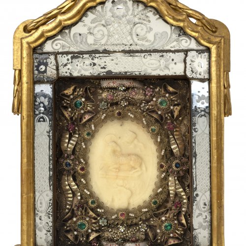Klosterarbeit mit Agnus-Dei-Wachsmedaillon, Rahmen mit Spiegelglaseinlagen, Empirschleifenbekrönung, 58 x 32 cm.